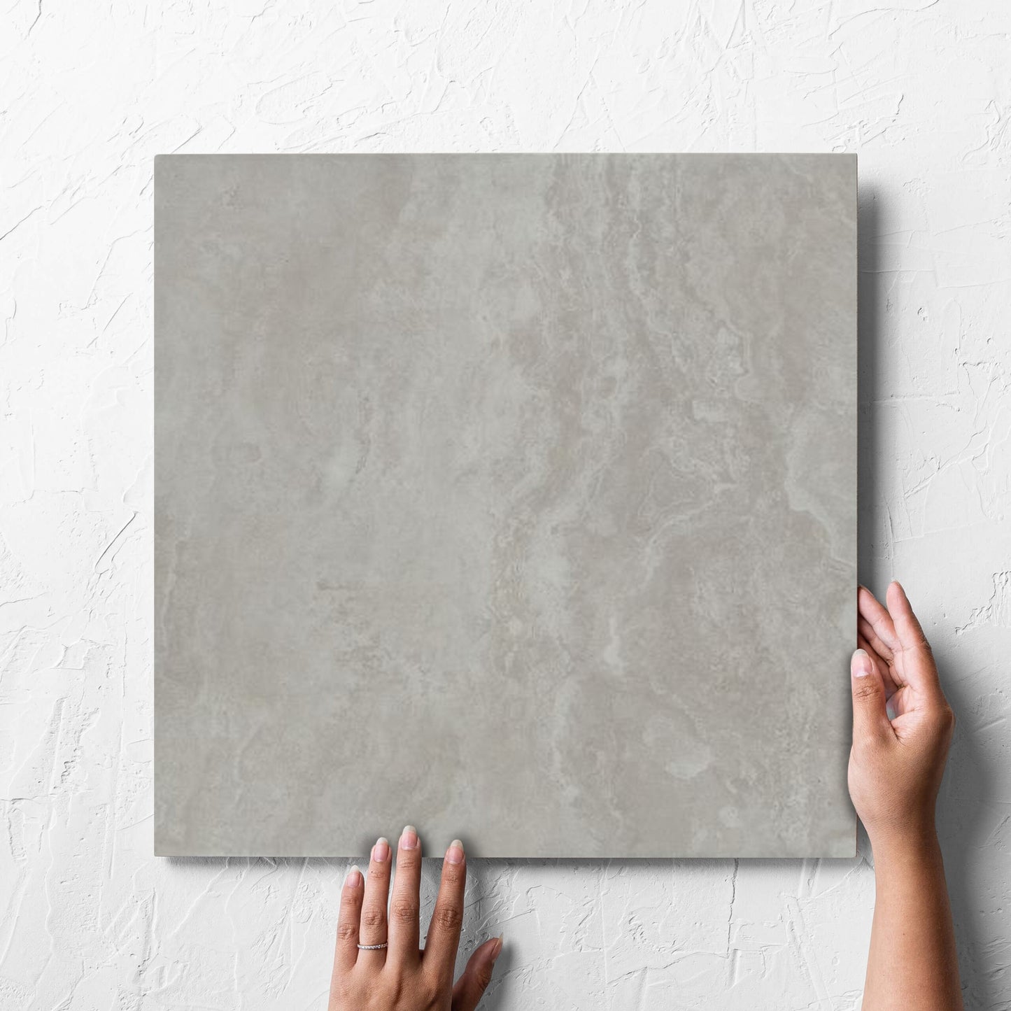 Hand holding a single Tivoli Grey Grip 450x450mm tile against a white rendered wall, showing the matt surface