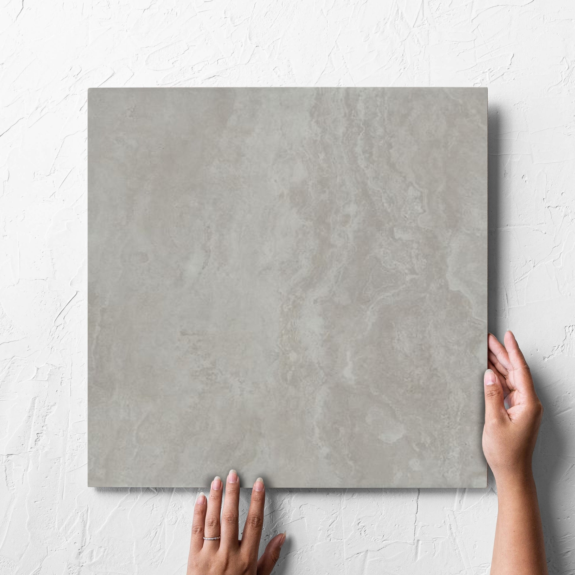 Hand holding a single Tivoli Grey Grip 450x450mm tile against a white rendered wall, showing the matt surface