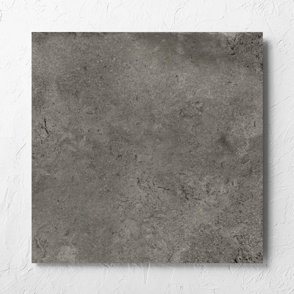 Toulouse Dark Grey Amber 600x600mm tile laid flat on a white rendered wall, showing the matt surface