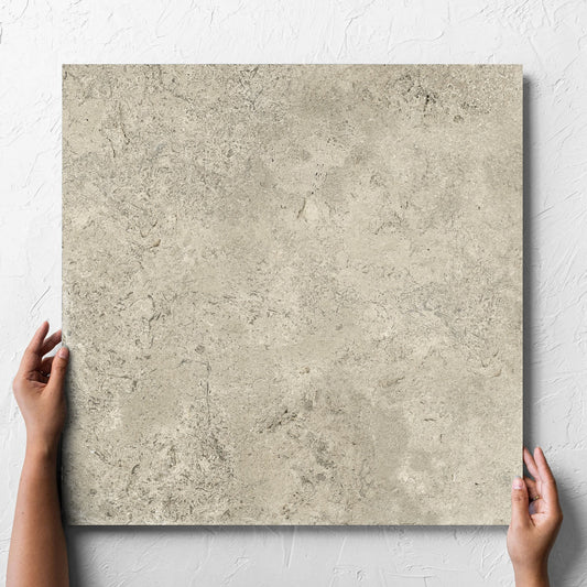 Hand holding a single Toulouse Natural Amber 600x600mm tile against a white rendered wall, showing the matt surface