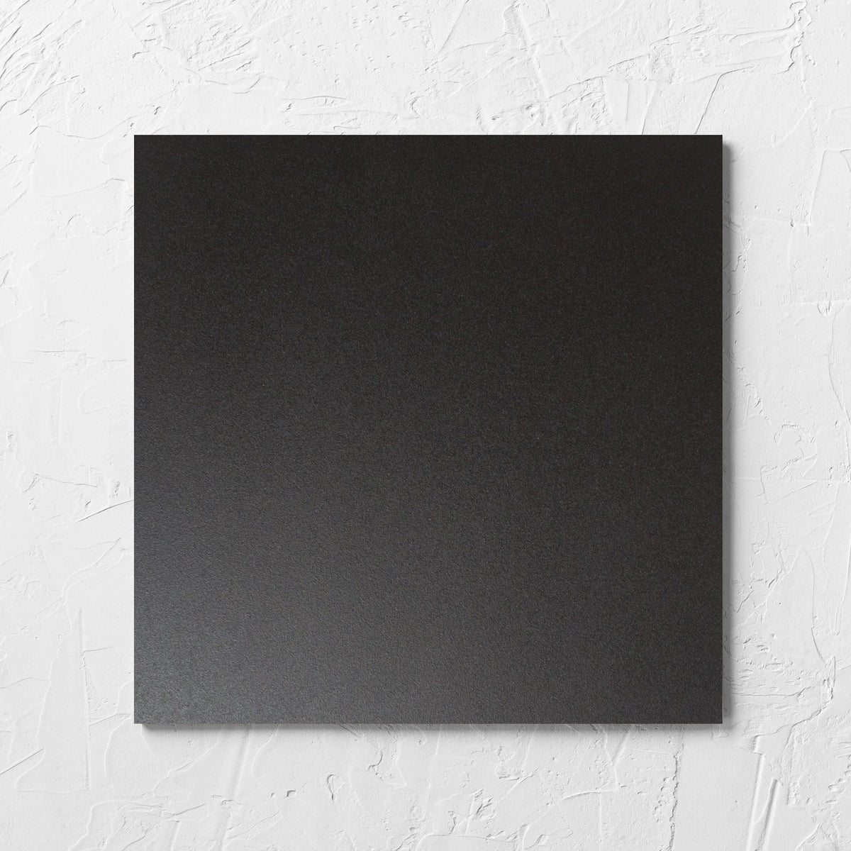 Unicolour Black Matt 300x300mm tile laid flat on a white rendered wall, showing the black matt surface