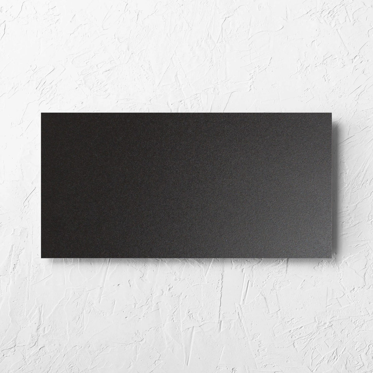 Unicolour Black Matt 300x600mm tile laid flat on a white rendered wall, showing the black matt surface