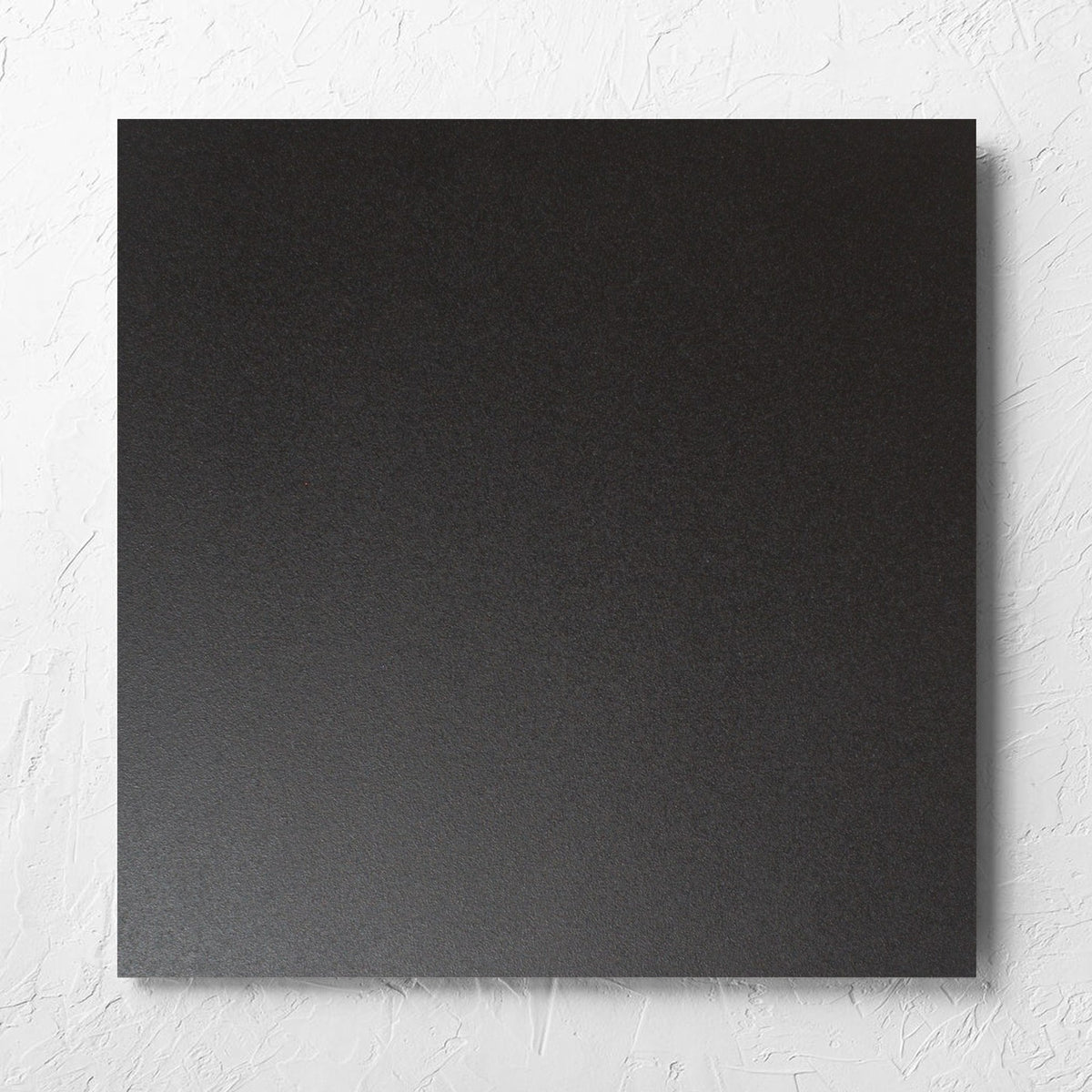 Unicolour Black Matt 600x600mm tile laid flat on a white rendered wall, showing the black matt surface