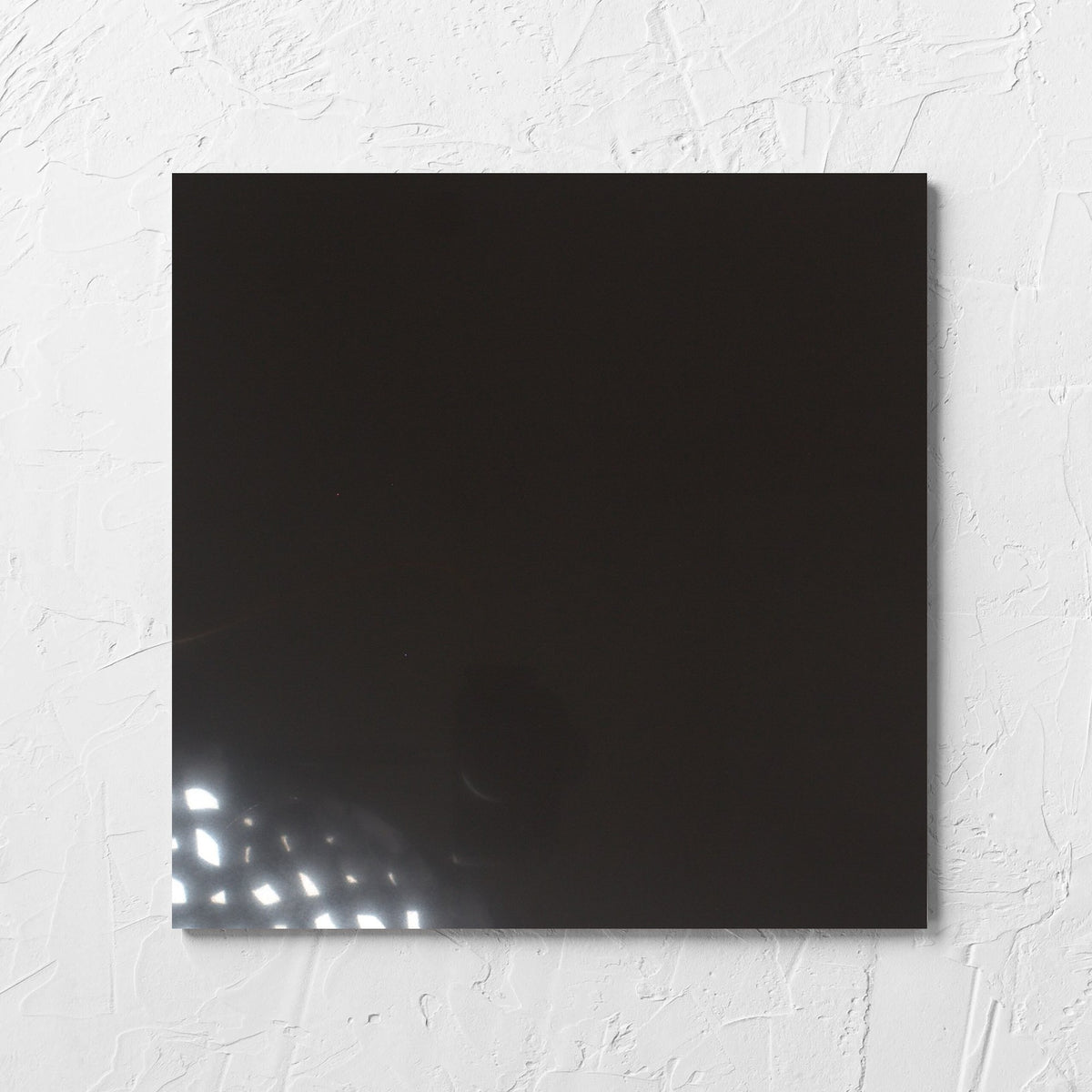 Unicolour Black Polished 300x300mm tile laid flat on a white rendered wall, showing the black polished surface