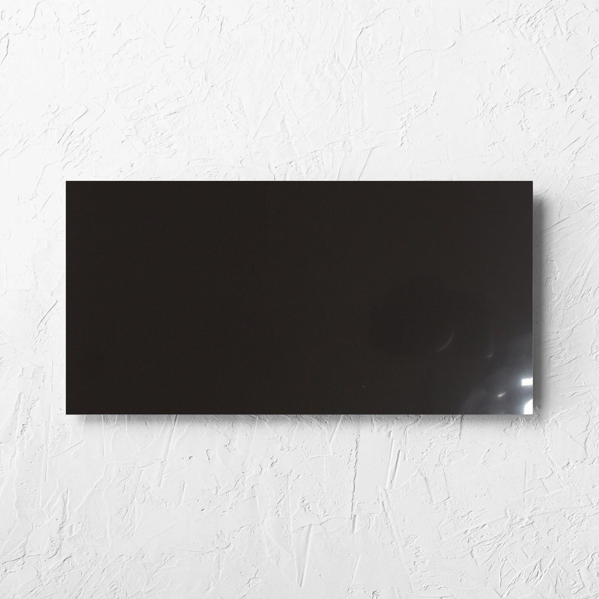 Unicolour Black Polished 300x600mm tile laid flat on a white rendered wall, showing the black polished surface