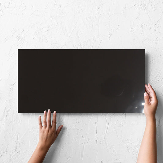 Hand holding a single Unicolour Black Polished 300x600mm tile against a white rendered wall, showing the black polished surface