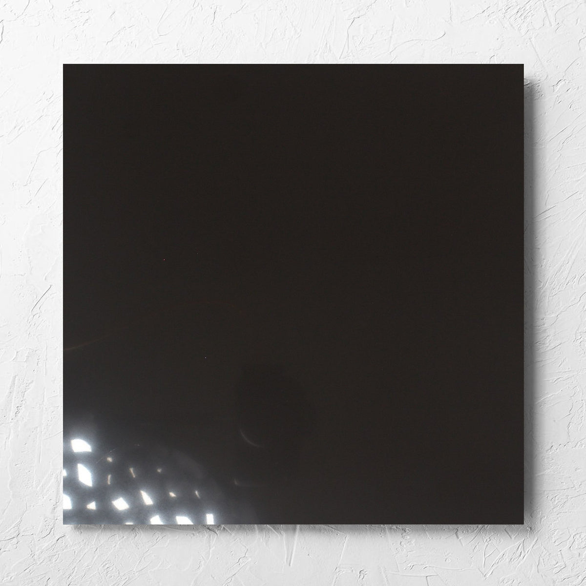 Unicolour Black Polished 600x600mm tile laid flat on a white rendered wall, showing the black polished surface