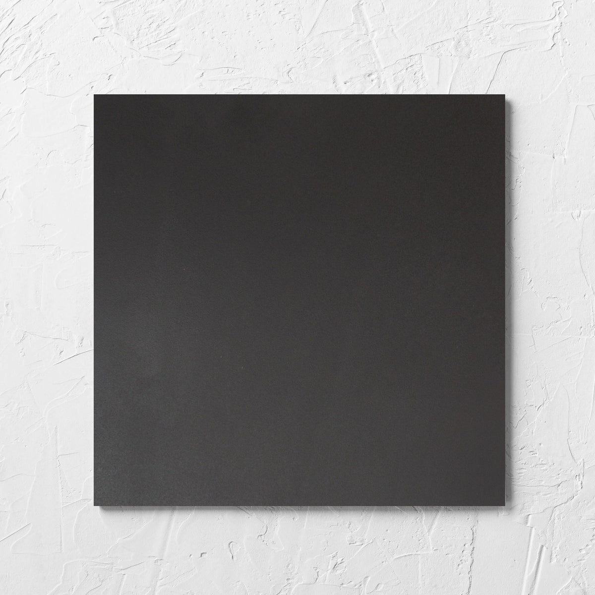 Unicolour Black R11 300x300mm tile laid flat on a white rendered wall, showing the black r11 surface