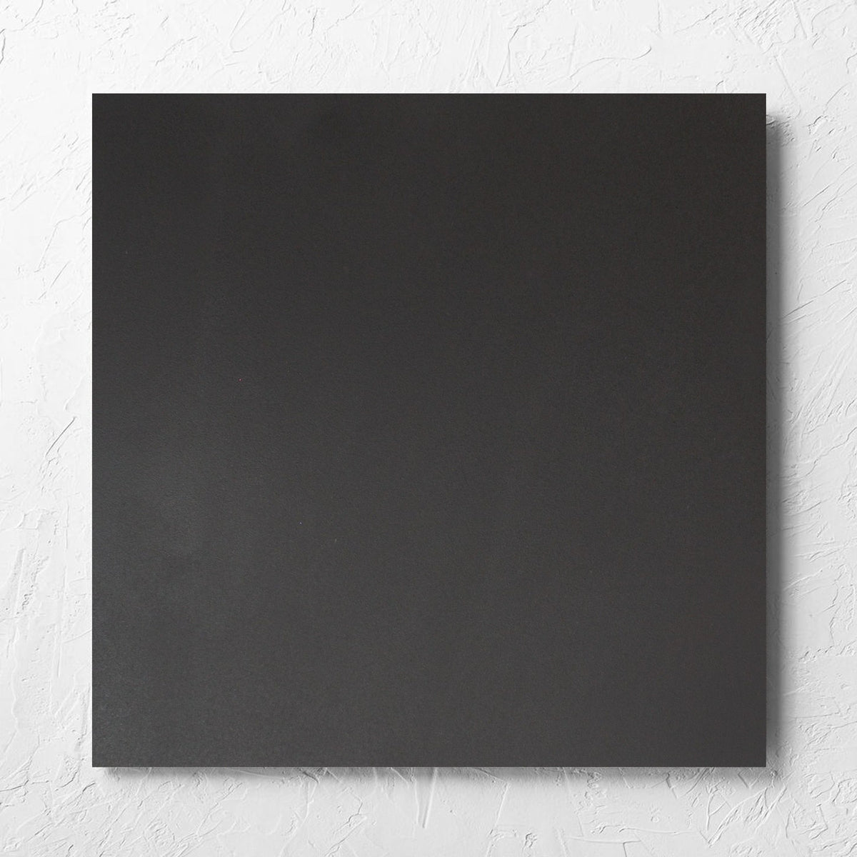 Unicolour Black R11 600x600mm tile laid flat on a white rendered wall, showing the black r11 surface