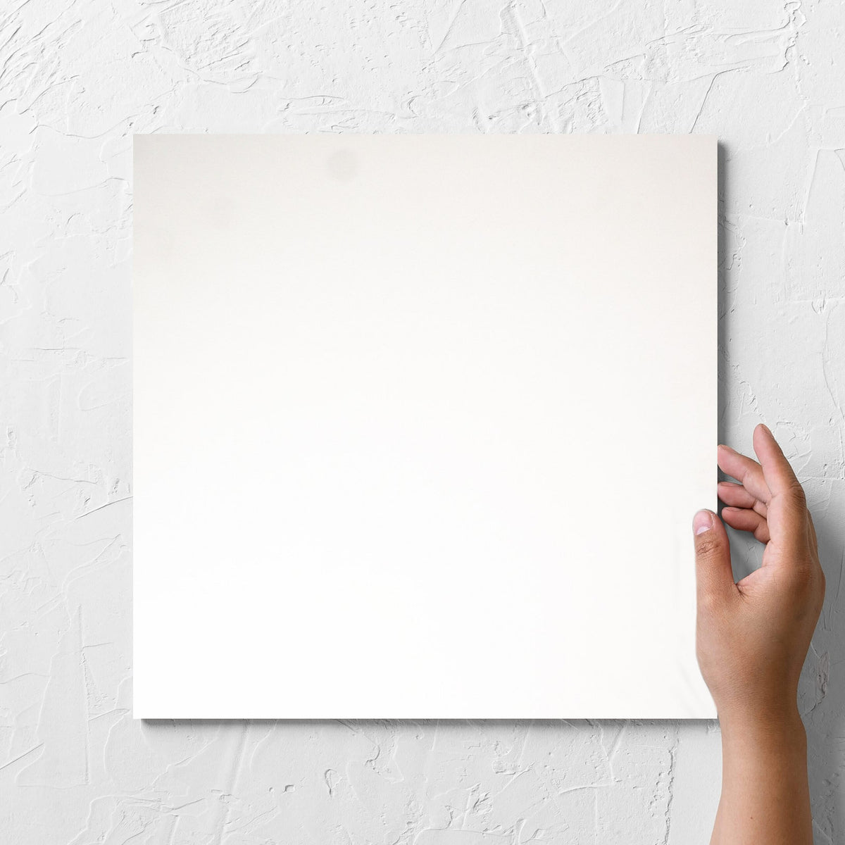 Hand holding a single Unicolour Super White Matt 300x300mm tile against a white rendered wall, showing the super white matt surface