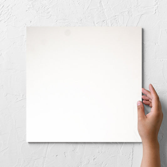 Hand holding a single Unicolour Super White Matt 300x300mm tile against a white rendered wall, showing the super white matt surface