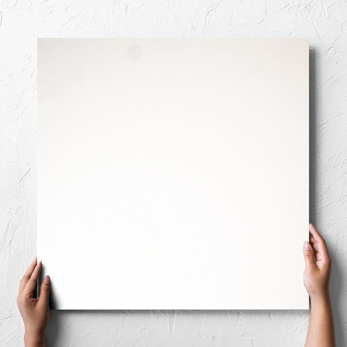 Hand holding a single Unicolour Super White Matt 600x600mm tile against a white rendered wall, showing the super white matt surface