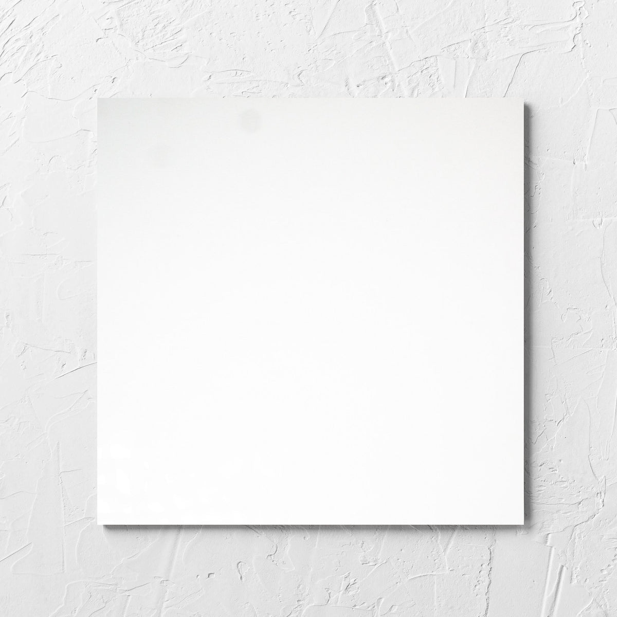 Unicolour White Polished 300x300mm tile laid flat on a white rendered wall, showing the white polished surface