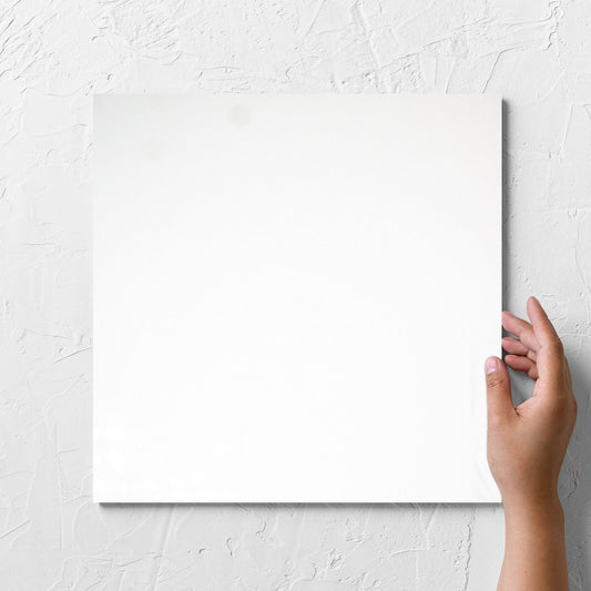 Hand holding a single Unicolour White Polished 300x300mm tile against a white rendered wall, showing the white polished surface