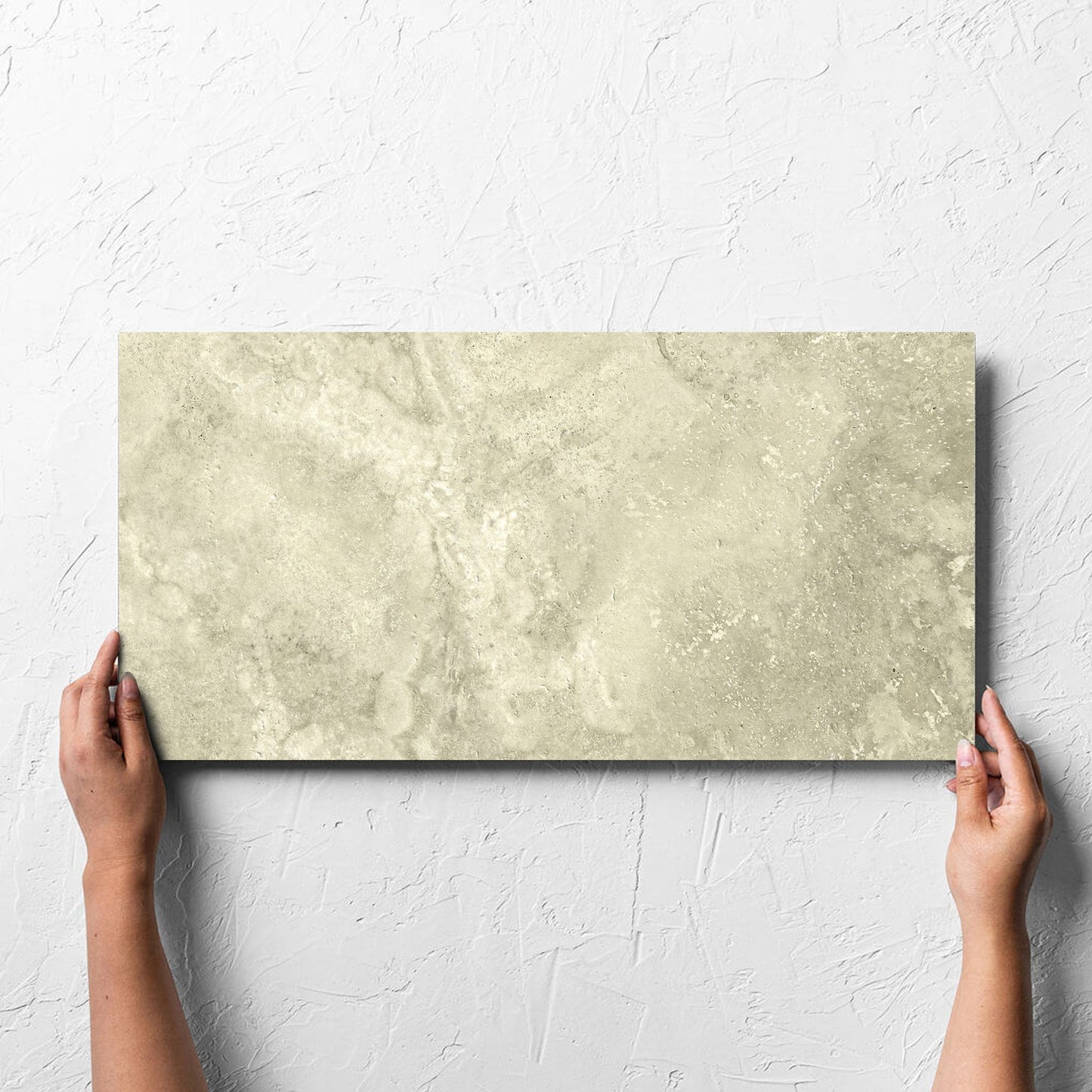 Hand holding a single Vatican Novona Cross Cut Travertine 300x600mm tile against a white rendered wall, showing the matt surface