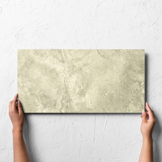 Hand holding a single Vatican Novona Cross Cut Travertine 300x600mm tile against a white rendered wall, showing the matt surface