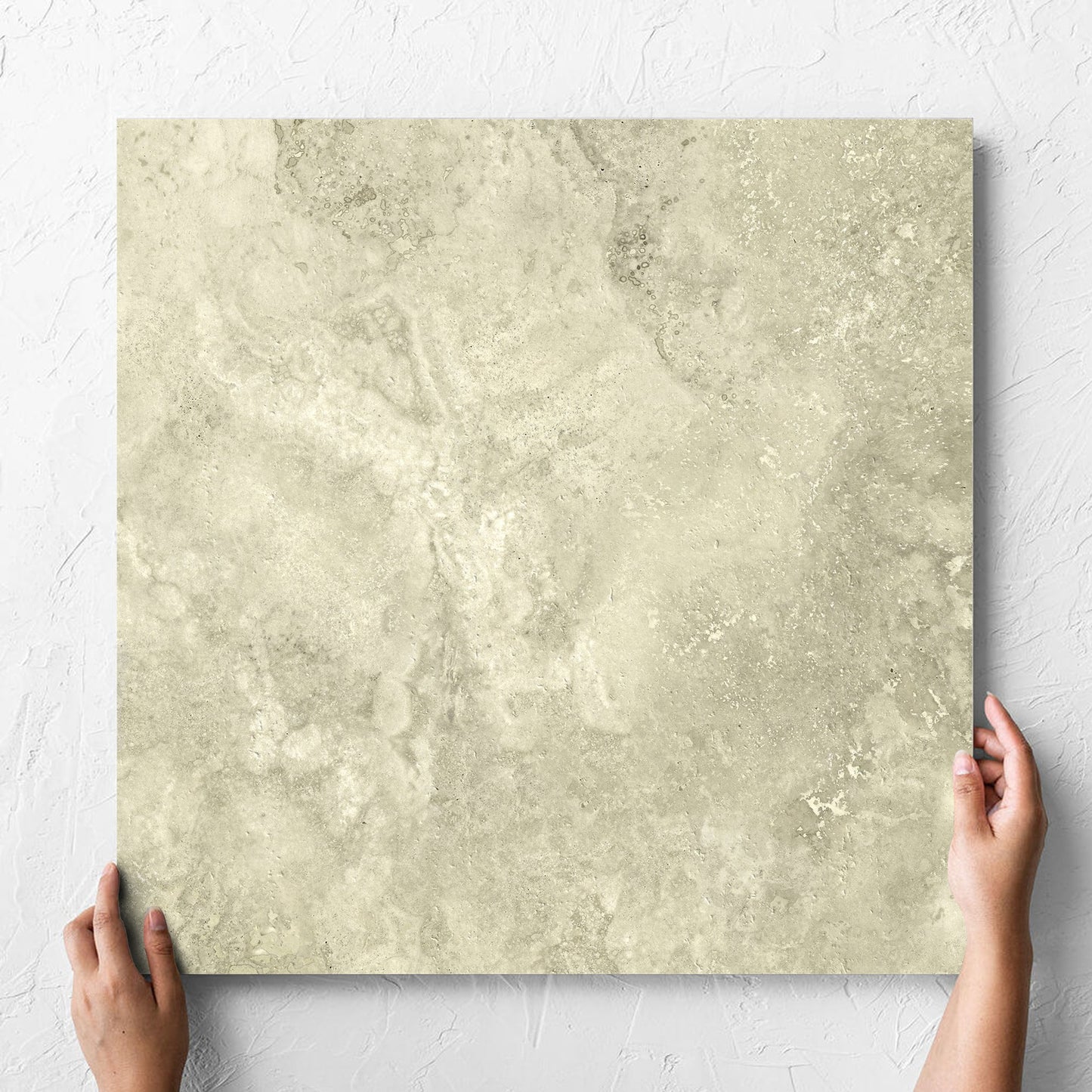 Hand holding a single Vatican Novona Cross Cut Travertine 600x600mm tile against a white rendered wall, showing the matt surface