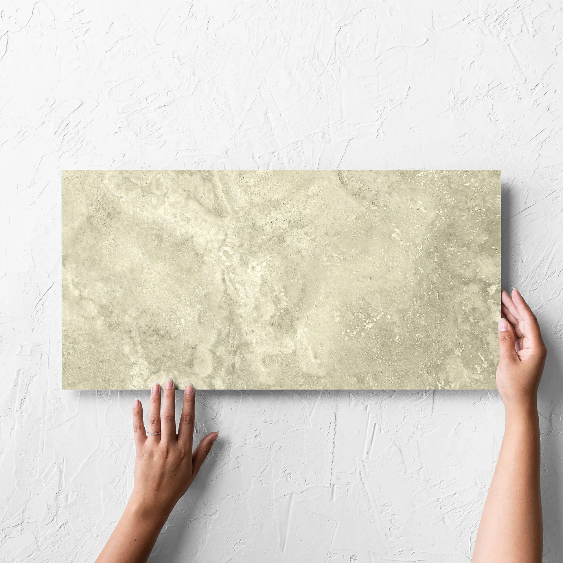 Hand holding a single Vatican Novona Vein Cut Travertine 300x600mm tile against a white rendered wall, showing the matt surface
