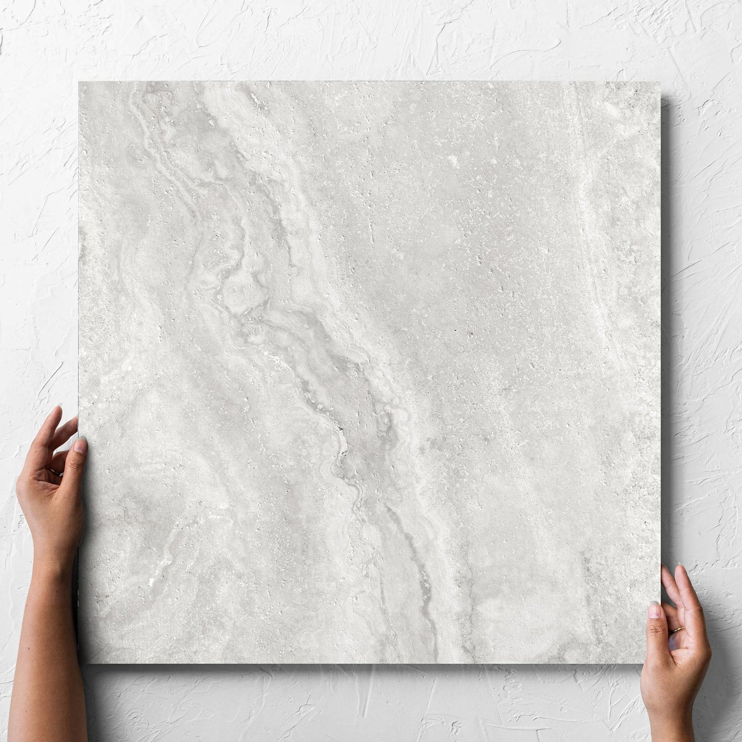 Hand holding a single Vatican Silver Vein Cut Travertine 600x600mm tile against a white rendered wall, showing the matt surface