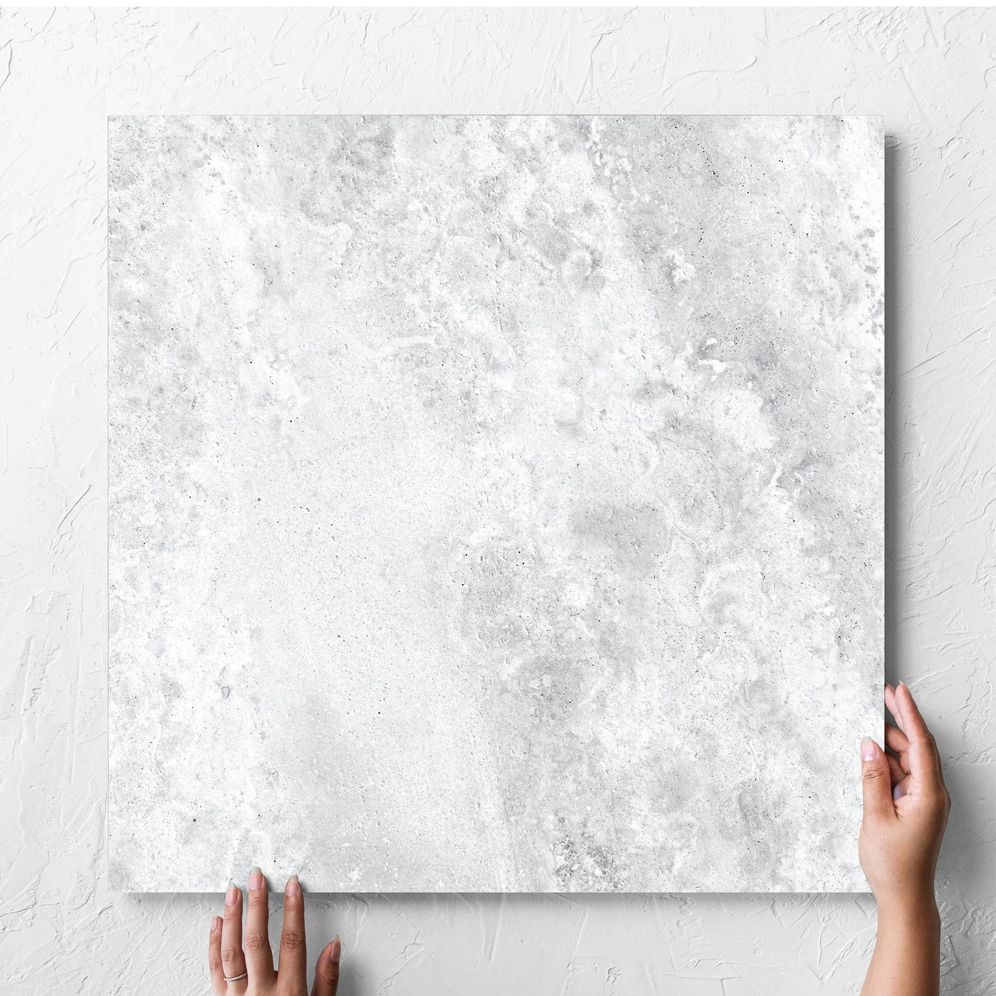 Hand holding a single Vatican White Cross Cut Travertine 600x600mm tile against a white rendered wall, showing the matt surface
