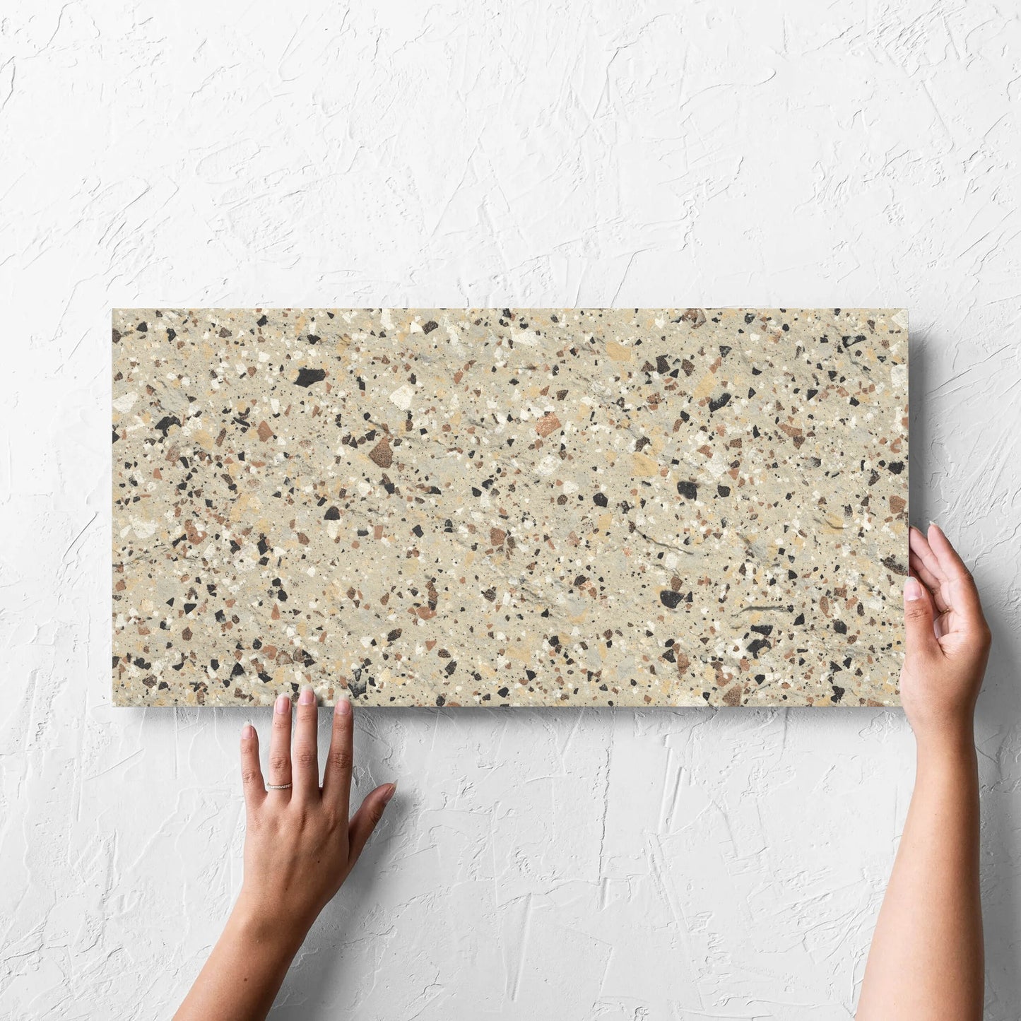 Hand holding a single Venice Beige 300x600mm Matt Terrazzo External Tile against a white rendered wall, showing the beige matt surface