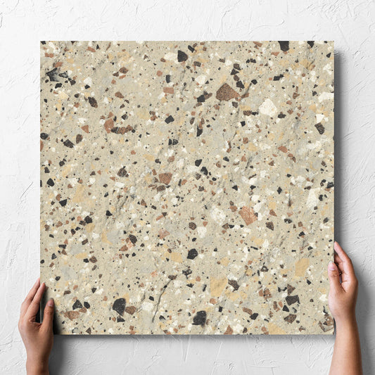 Hand holding a single Venice Beige 600x600mm Matt Terrazzo External Tile against a white rendered wall, showing the beige matt surface