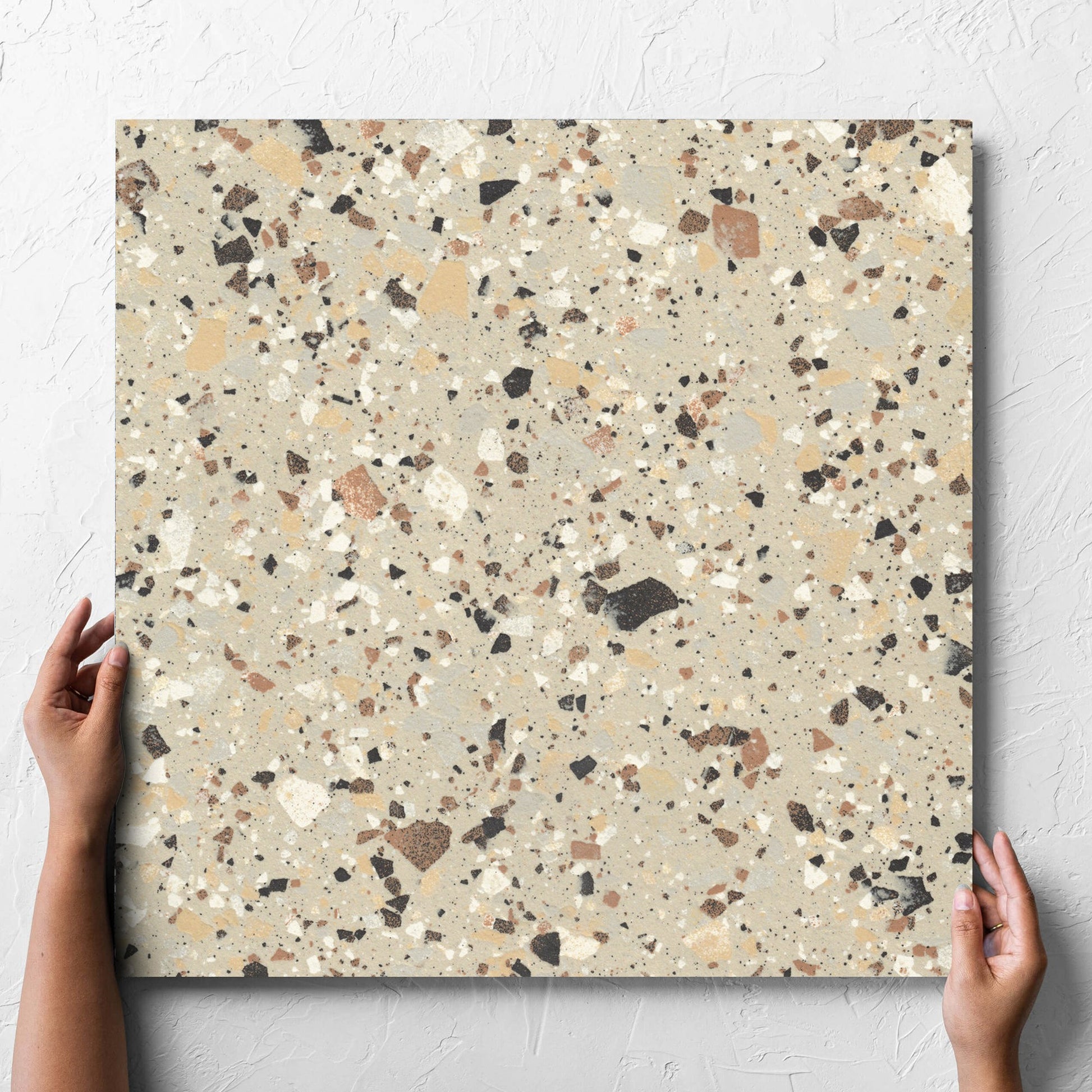 Hand holding a single Venice Beige 600x600mm Matt Terrazzo Tile against a white rendered wall, showing the beige matt surface