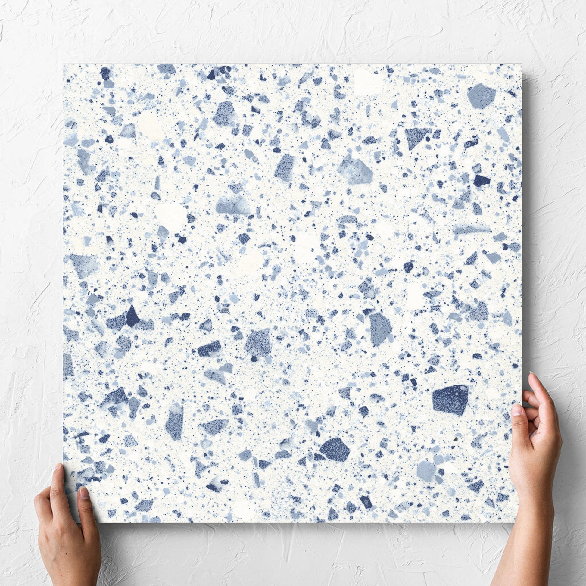Hand holding a single Venice Blue 600x600mm Matt Terrazzo Tile against a white rendered wall, showing the blue matt surface