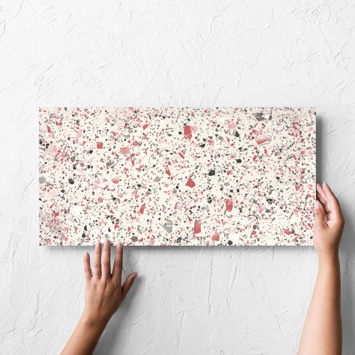 Hand holding a single Venice Coral 300x600mm Matt Terrazzo Tile against a white rendered wall, showing the coral matt surface