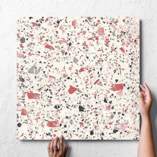 Hand holding a single Venice Coral 600x600mm Matt Terrazzo Tile against a white rendered wall, showing the coral matt surface