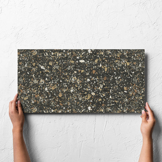 Hand holding a single Venice Earth 300x600mm Matt Terrazzo External Tile against a white rendered wall, showing the earth matt surface