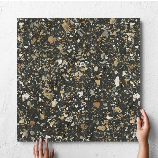 Hand holding a single Venice Earth 600x600mm Matt Terrazzo External Tile against a white rendered wall, showing the earth matt surface