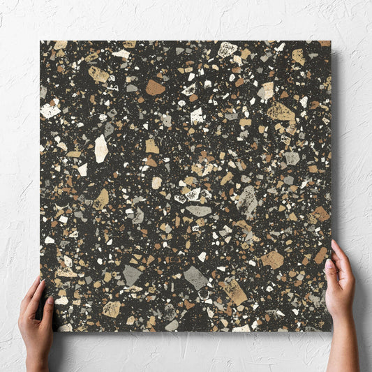 Hand holding a single Venice Earth 600x600mm Matt Terrazzo Tile against a white rendered wall, showing the earth matt surface