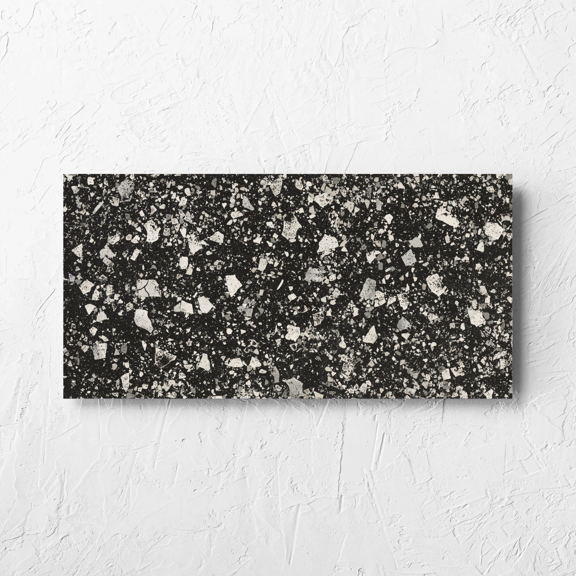 Venice Graphite 300x600mm Matt Terrazzo Tile laid flat on a white rendered wall, showing the graphite matt surface