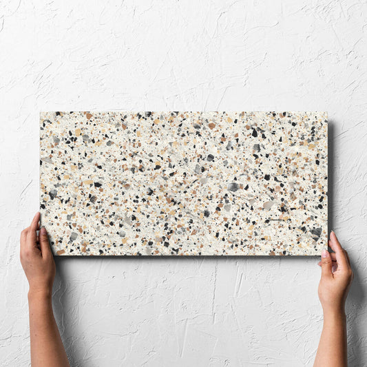 Hand holding a single Venice Ivory 300x600mm Matt Terrazzo External Tile against a white rendered wall, showing the ivory matt surface