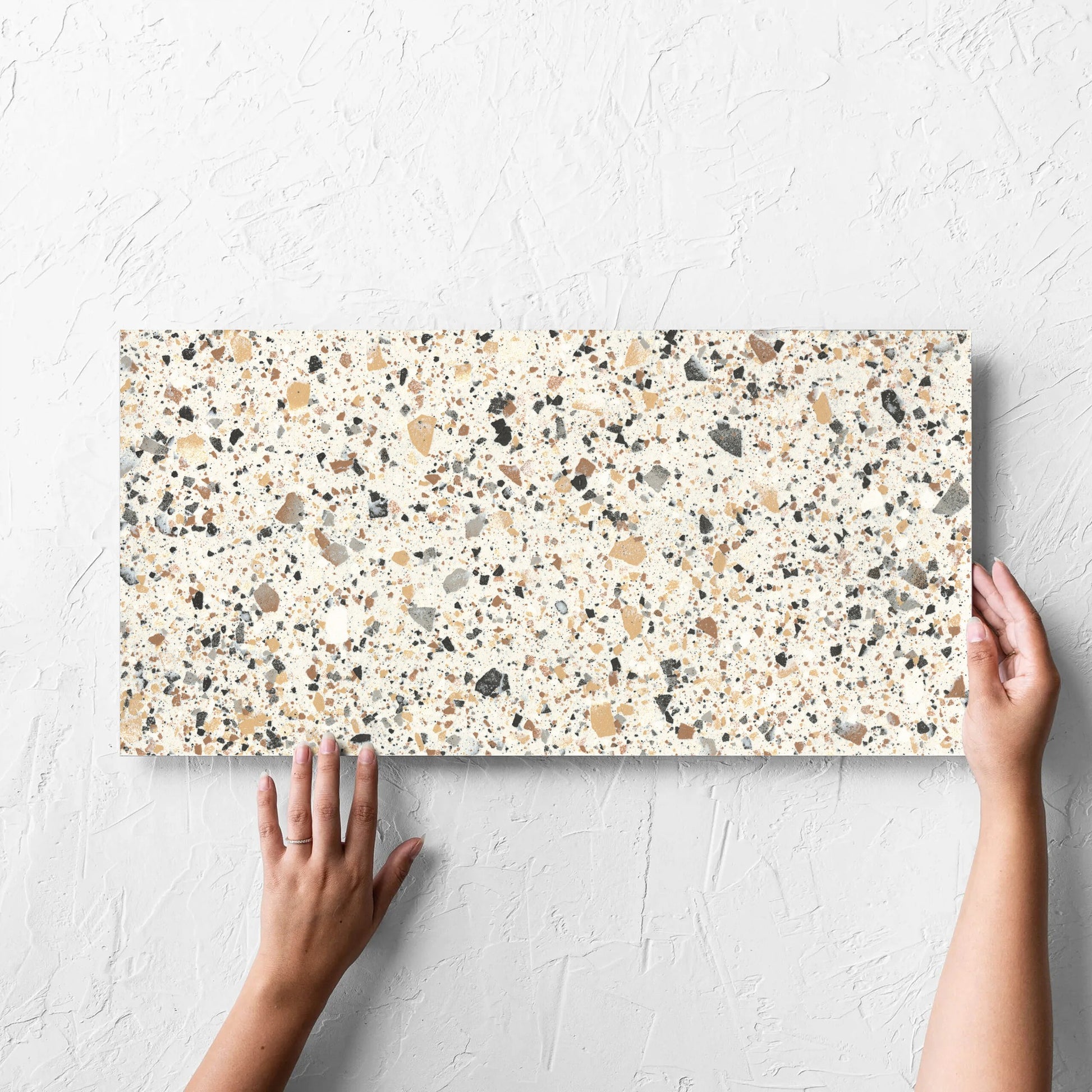 Hand holding a single Venice Ivory 300x600mm Matt Travertine Look Tile tile against a white rendered wall, showing the tile surface