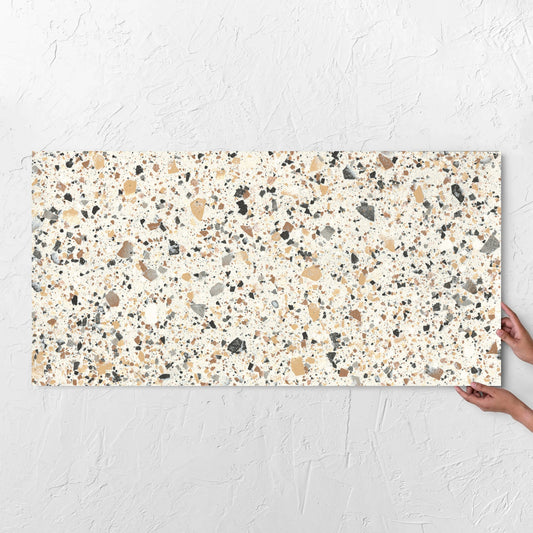 Hands holding a Venice Ivory 600x1200mm Matt Terrazzo Tile against a white rendered wall, showing the ivory matt surface