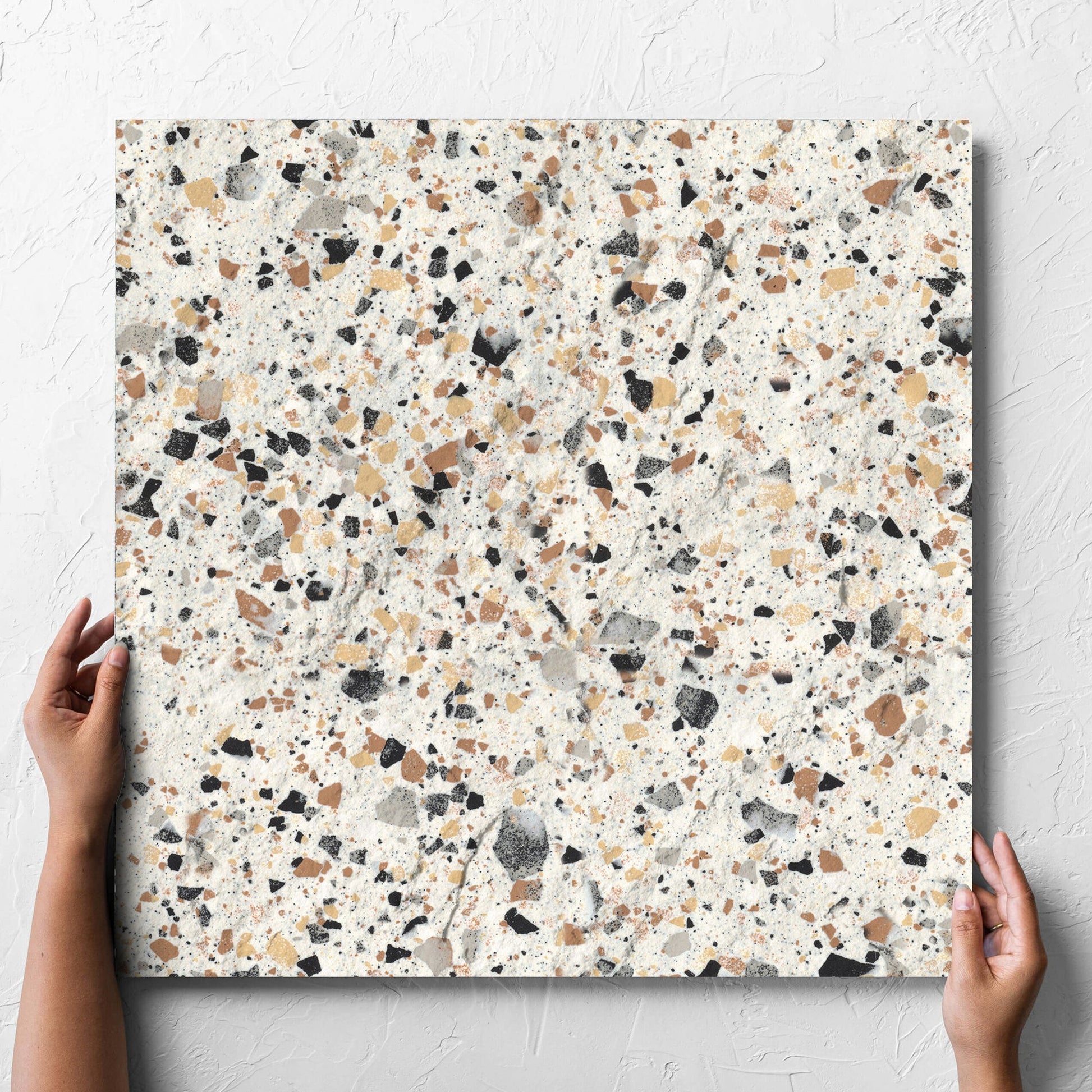 Hand holding a single Venice Ivory 600x600mm Matt Terrazzo External Tile against a white rendered wall, showing the ivory matt surface