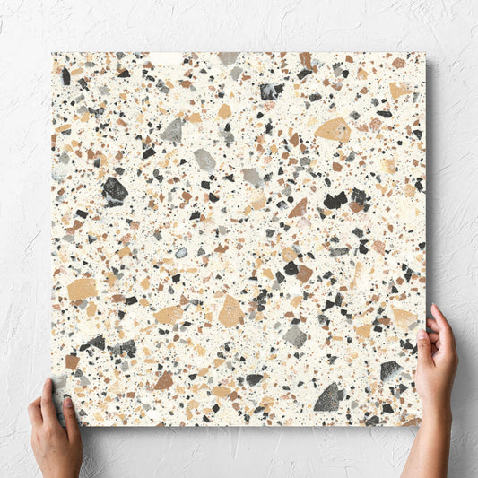 Hand holding a single Venice Ivory 600x600mm Matt Terrazzo Tile against a white rendered wall, showing the ivory matt surface