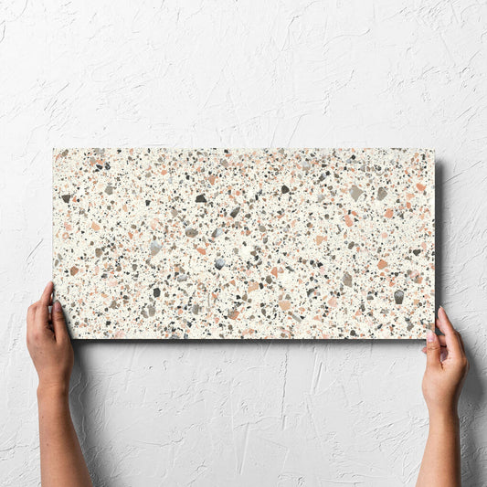 Hand holding a single Venice Pink 300x600mm Matt Terrazzo Tile against a white rendered wall, showing the pink matt surface