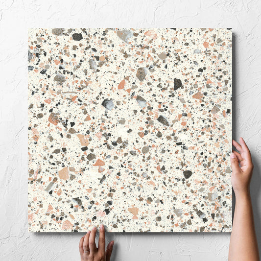 Hand holding a single Venice Pink 600x600mm Matt Terrazzo Tile against a white rendered wall, showing the pink matt surface