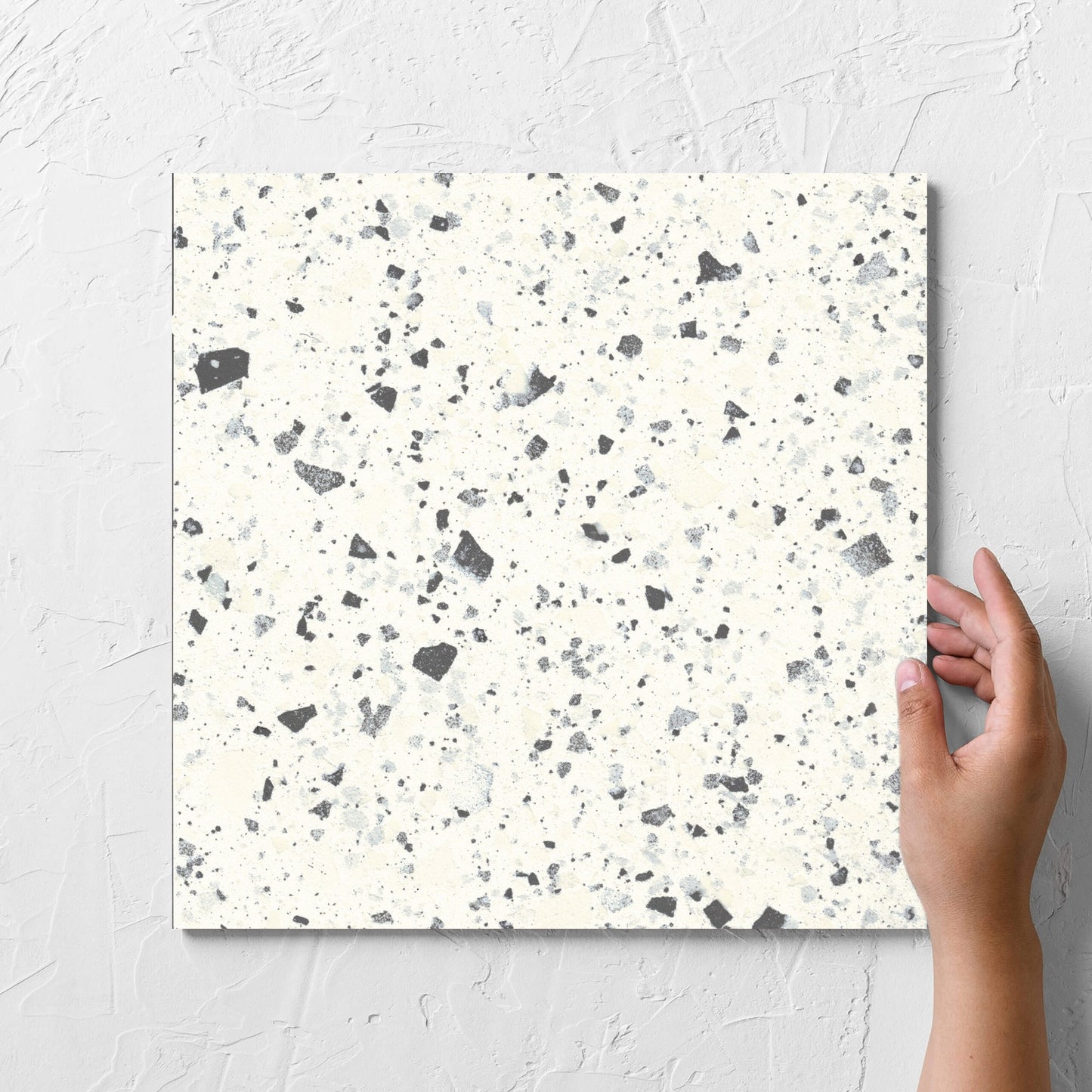 Hand holding a single Venice White 300x300mm Matt Terrazzo Tile against a white rendered wall, showing the white matt surface
