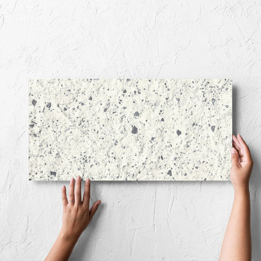 Hand holding a single Venice White 300x600mm Matt Terrazzo External Tile against a white rendered wall, showing the white matt surface