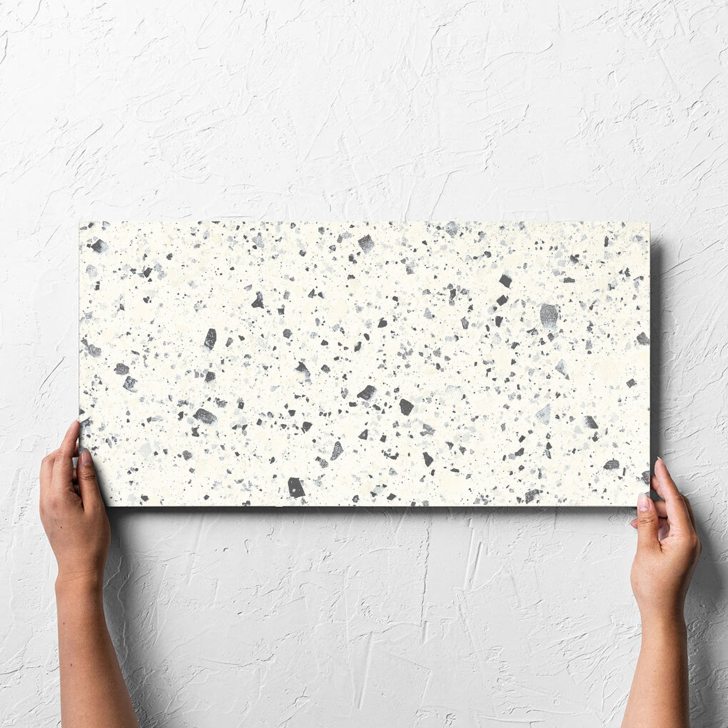 Hand holding a single Venice White 300x600mm Matt Terrazzo Tile against a white rendered wall, showing the white matt surface