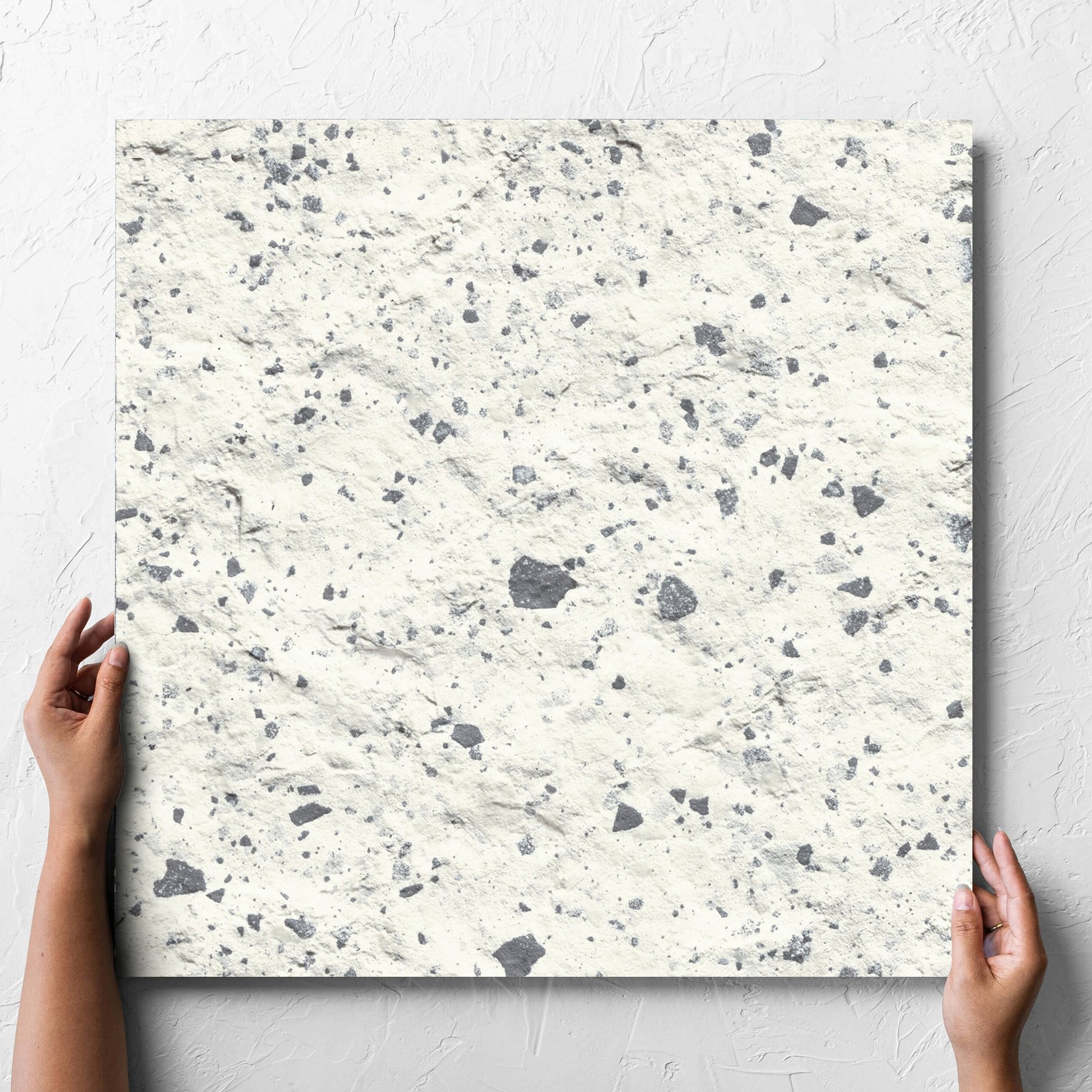Hand holding a single Venice White 600x600mm Matt Terrazzo External Tile against a white rendered wall, showing the white matt surface