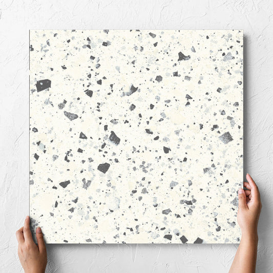 Hand holding a single Venice White 600x600mm Matt Terrazzo Tile against a white rendered wall, showing the white matt surface