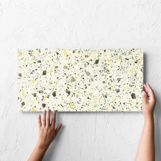 Hand holding a single Venice Yellow 300x600mm Matt Terrazzo Tile against a white rendered wall, showing the yellow matt surface