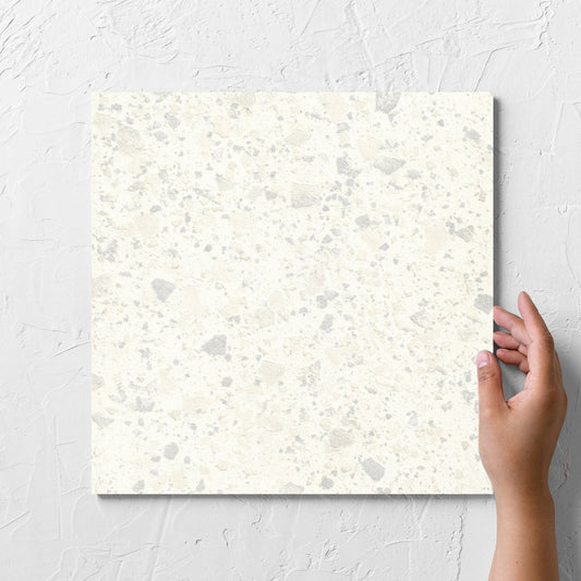 Hand holding a single Venice Zinc 300x300mm Matt Terrazzo Tile against a white rendered wall, showing the zinc matt surface