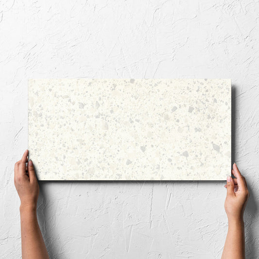 Hand holding a single Venice Zinc 300x600mm Matt Terrazzo Tile against a white rendered wall, showing the zinc matt surface