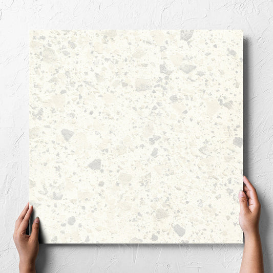 Hand holding a single Venice Zinc 600x600mm Matt Terrazzo Tile against a white rendered wall, showing the zinc matt surface